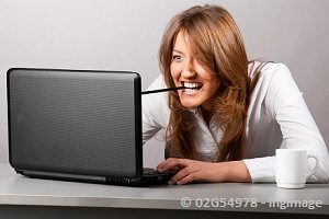 girl typing on computer with a pencil in her teeth