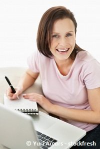 girl writing something on a notepad while sitting in front of the laptop